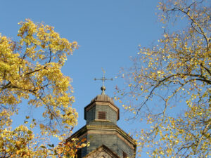 Bosseborner Kirche. Der Kirchturm mit Bäumen im Herbst bei strahlend blauem Himmel